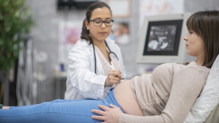 ibu hamil A pregnant woman and her female doctor are indoors in a hospital. The doctor is performing an ultrasound.