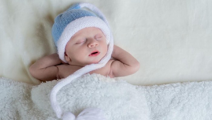 Newborn baby boy sleeping and dreaming with arms behind his head
