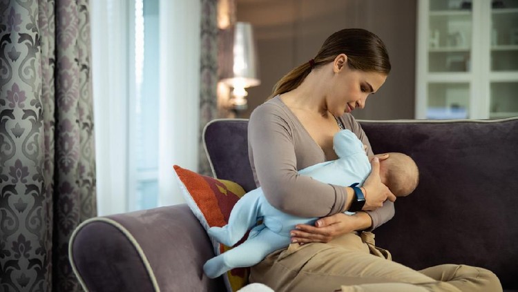Happy woman giving breast milk to her newborn baby while sitting in living room stock photo
