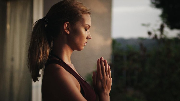 Namaste gesture close up photo, young attractive woman practicing yoga, working out, wearing wrist bracelets and rings, indoor, yoga studio, behind the shoulder view. Contemplation concept
