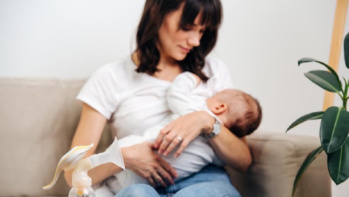 breast pump on the table, in the background mother breastfeeds the baby