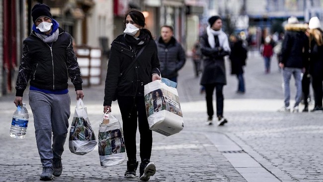 People wear protective face masks as they carry groceries in the centre of Brussels, amid the outbreak of COVID-19, caused by the novel coronavirus. - Belgium close schools, cancel all cultural events and shutter bars and restaurants to stave off the spread of the coronavirus outbreak.  Beginning on March 14, only stores that provide essential services -- such as pharmacies and grocery stores-- will remain open under normal conditions. (Photo by Kenzo TRIBOUILLARD / AFP)