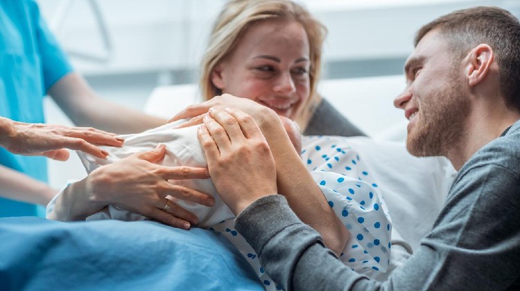 melahirkan caesar In the Hospital Midwife Gives Newborn Baby to a Mother to Hold, Supportive Father Lovingly Hugging Baby and Wife. Happy Family in the Modern Delivery Ward.
