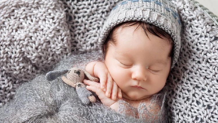 Sweet newborn baby sleeps in a basket. Beautiful newborn boy with bear toy.