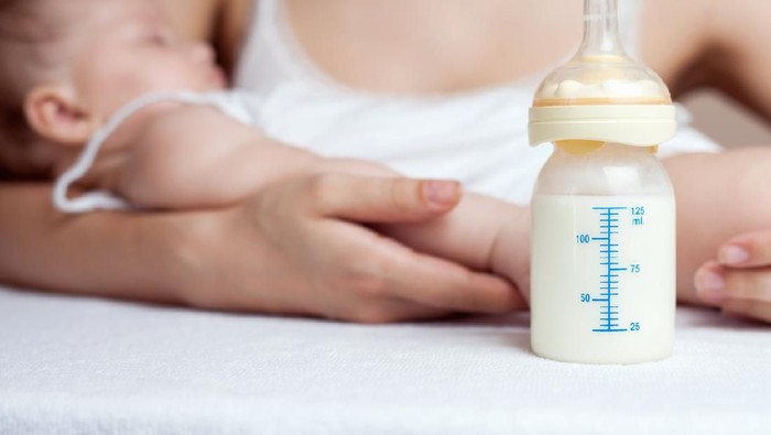 Mother holding a baby and bottle with breast milk for breastfeeding at foreground, mothers breast milk is the most healthy food for newborn baby