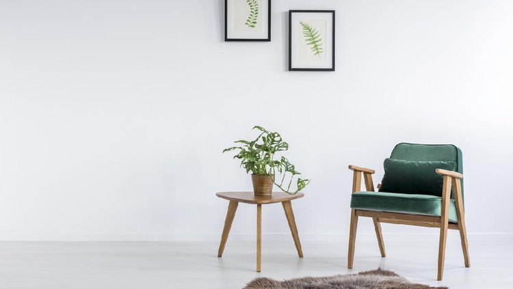 White apartment interior showing comfortable living room sofa on the left, and a wooden dining table with colorful chairs. There are windows showing green nature scenery. Yellow details. Concrete polished floor with wooden coffee table. Lots of decorative details. Horizontal composition