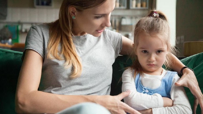 Angry offended little girl ignoring not listening mother words, advice, mum hugging, talking with stubborn, upset daughter at living room, bad upbringing, difficult behavior of child