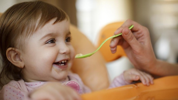Mother feeding happy toddler girl with a spoon
