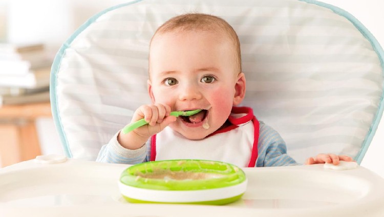 Mother feeding happy toddler girl with a spoon