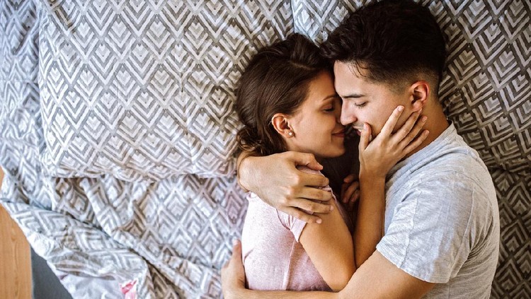 Young couple in love lying on bed at home and cuddling, embracing and enjoying weekend together