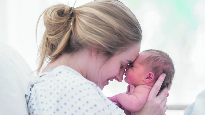 Young mother, holding her sick toddler boy, breastfeeding him at home, sunny living room