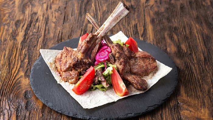 ribeye steak on the bone, tomahawk, served with tomatoes and iceberg lettuce on pita on slate board.