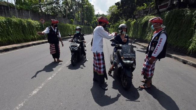 Pecalang atau petugas keamanan adat Bali memeriksa sejumlah warga yang melintas di Tabanan, Bali, Kamis (26/3/2020). Penjagaan dilakukan di setiap perbatasan desa / kota dengan melibatkan unsur pecalang, TNI dan Polri untuk mengurangi lalu lalang orang pascaimbauan gubernur Bali agar masyarakat tetap berada di rumah untuk  mencegah penyebaran COVID-19. ANTARA FOTO/Nyoman Hendra Wibowo/nym/am