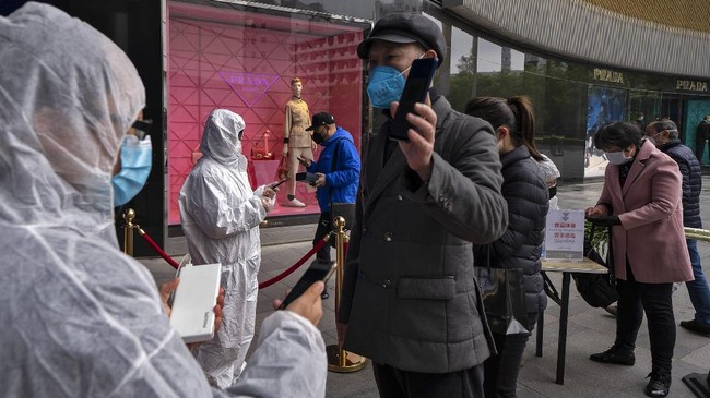 In this photo released by Xinhua News Agency, workers wearing protective suits check customers' health QR codes at the entrance of a re-opened shopping mall in in Wuhan in central China's Hubei province, Monday, March 30, 2020. Shopkeepers in the city at the center of China's virus outbreak were reopening Monday but customers were scarce after authorities lifted more of the anti-virus controls that kept tens of millions of people at home for two months. (Fei Maohua/Xinhua via AP)
