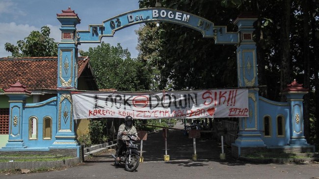 Warga melintas di depan spanduk penutupan jalan masuk Desa Bogem, Kalasan, Sleman, DI Yogyakarta, Senin (30/3/2020). Sejumlah desa atau perkampungan di Kota dan Kabupaten di DI Yogyakarta memberlakukan akses satu pintu masuk dengan menutup sejumlah jalan untuk mengurangi aktivitas warga sebagai upaya mencegah penularan COVID-19. ANTARA FOTO/Hendra Nurdiyansyah/aww.