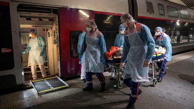 Medical staff carry a patient infected with the COVID-19 into a TGV high speed train at the Gare d'Austerlitz train station on April 1, 2020 in Paris, prior to his evacuation, along with 35 other patients in two separate medical TGV towards hospitals of Brittany, western France, where the outbreak of the Covid-19 pandemic caused by the novel coronavirus where has been limited so far. (Photo by Thomas SAMSON / POOL / AFP)