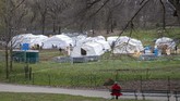 Dari kejauhan, seorang perempuan melihat anggota dan tenaga medis Dompet Samaritan tengah menyiapkan rumah sakit darurat di Centrak Park, salah satu taman kota terbesar di kota New York, Amerika Serikat. (AP Photo/Mary Altaffer)
