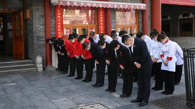 Restaurant staff members wearing face masks mourn patients and medical staff killed by coronavirus during a nationwide three minutes silence along a business street in Beijing on April 4, 2020. - China came to a standstill to mourn patients and medical staff killed by the coronavirus, with the world's most populous country observing a nationwide three-minute silence. (Photo by WANG ZHAO / AFP)