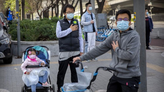 People stand along a street during a national moment of mourning for victims of the coronavirus, in Beijing, Saturday, April 4, 2020. With air raid sirens wailing and flags at half-staff, China on Saturday held a three-minute nationwide moment of reflection to honor those who have died in the coronavirus outbreak, especially 