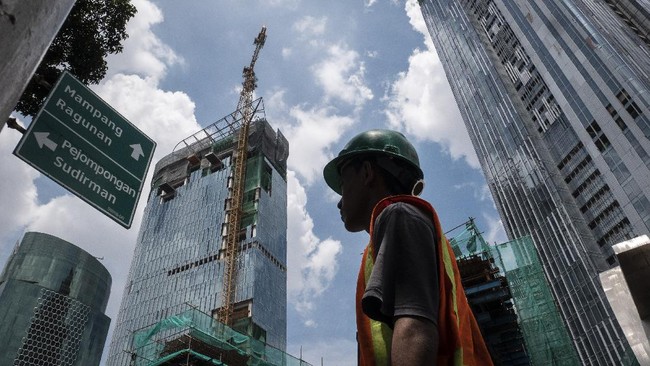 Pekerja melintas dengan latar belakang pembangunan gedung bertingkat di kawasan Kuningan, Jakarta, Jumat (3/4/2020). Bank Indonesia (BI) mengoreksi proyeksi pertumbuhan ekonomi Indonesia paling rendah 2,3 persen pada tahun ini yang akan ditopang oleh berbagai stimulus, baik fiskal maupun moneter yang diberikan oleh pemerintah dan bank sentral. ANTARA FOTO/Dhemas Reviyanto/pras.
