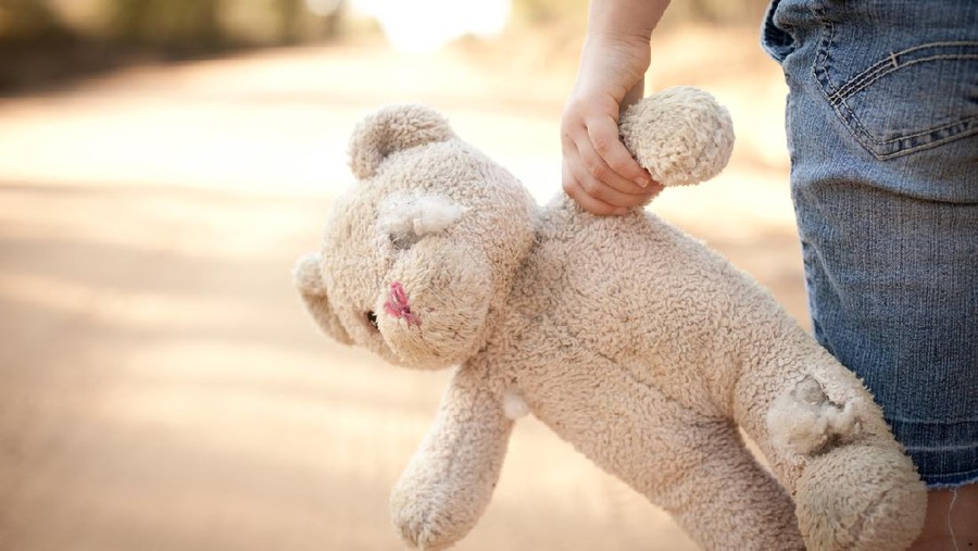 Color stock photo of a little runaway girl holding an old teddy bear at the side of a dirt road in the rural country.