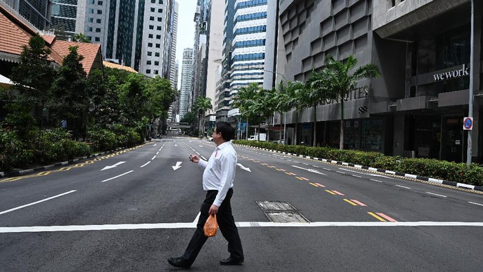 A man crosses an empty street in the central business district of Singapore on April 7, 2020, as the country ordered the closure of all businesses deemed non-essential as well as schools to combat the spread of the COVID-19 novel coronavirus. - Singapore's usually bustling business district was almost deserted on April 7 as most workplaces in the city-state closed to stem the spread of the coronavirus after a surge in cases. (Photo by Roslan RAHMAN / AFP)