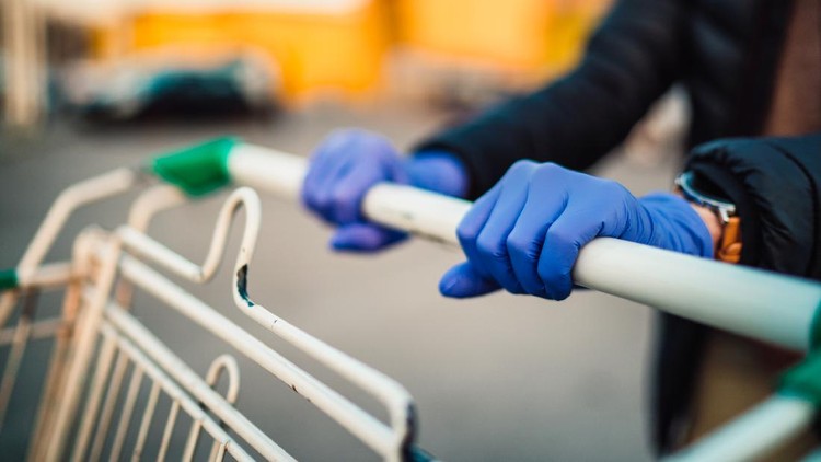 Close-up view of hands in rubber gloves pushing shopping carts in front of supermarket.