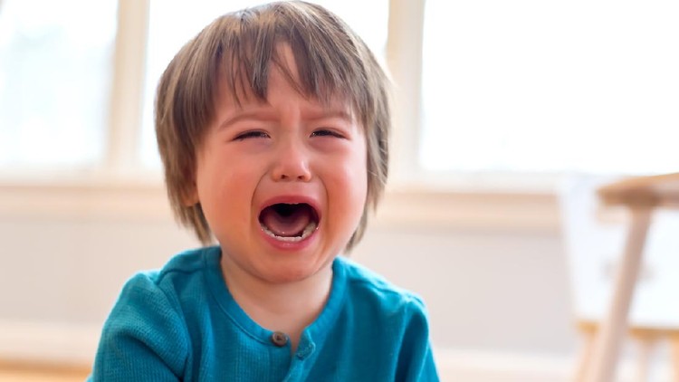 A mother holding a crying toddler daughter indoors in kitchen when cooking.