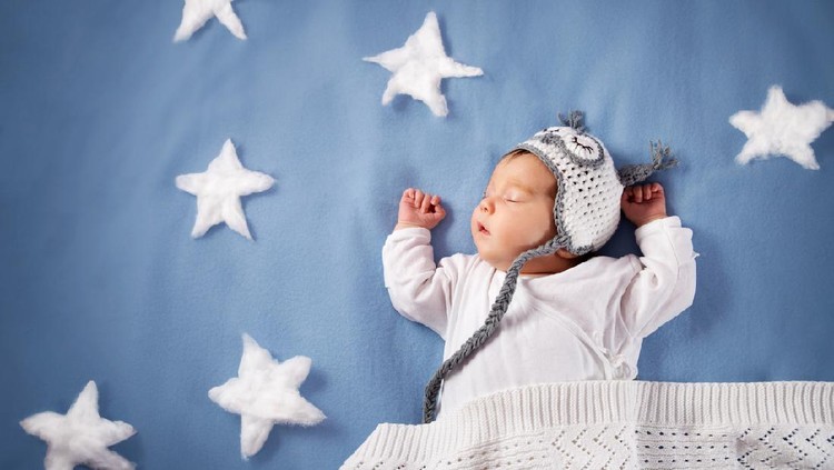 Cute newborn baby girl lying in the bed. 2 month old child in owl hat sleeping on blue blanket with stars