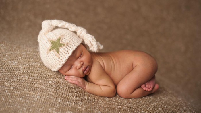 Cute newborn baby girl lying in the bed. 2 month old child in owl hat sleeping on blue blanket with stars