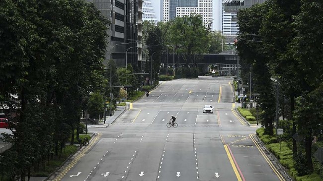 A cyclist rides across a quiet street in the central business district of Singapore on April 7, 2020, as the country ordered the closure of all businesses deemed non-essential as well as schools to combat the spread of the COVID-19 novel coronavirus. - Singapore's usually bustling business district was almost deserted on April 7 as most workplaces in the city-state closed to stem the spread of the coronavirus after a surge in cases. (Photo by Roslan RAHMAN / AFP)