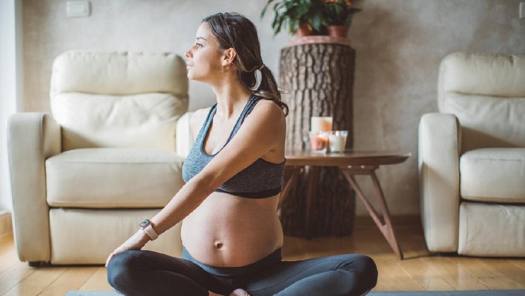 Young pregnant woman exercising at home. She workout on exercise mat and stretching.