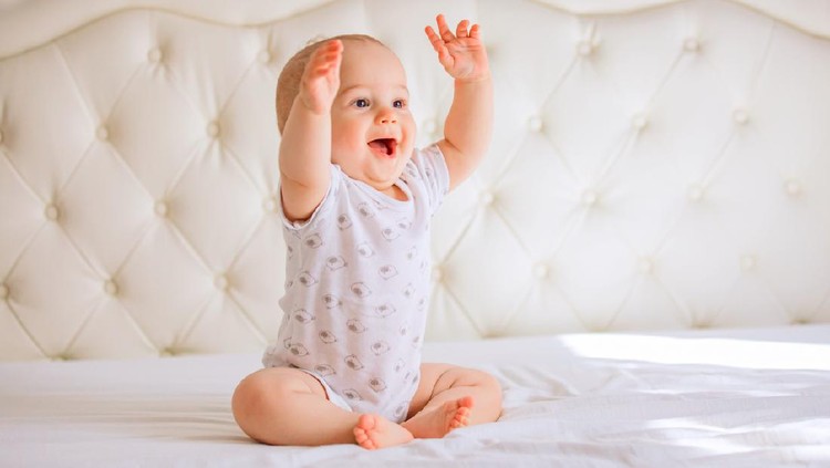 Cute baby boy in white sunny bedroom.