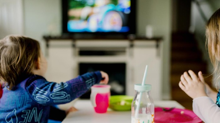 Siblings eating a meal at a child sized table and watching cartoons