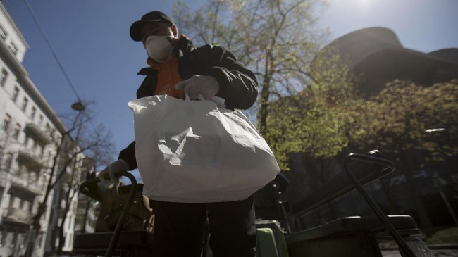 A horse-drawn carriage driver gets off with a meal package from fiaker in the 3rd district in Vienna, Austria on April 8, 2020. - The Hotel Intercontinental cooks up to 350 lunches a day for people in need who are unable to feed themselves due to the coronavirus pandemic. The meals are delivered voluntarily by fiaker drivers. (Photo by ALEX HALADA / AFP)