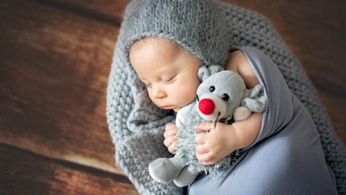 Little newborn baby boy, sleeping in basket, holding toy, posed picture