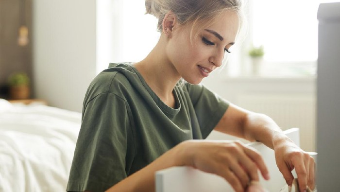 Pretty young housewife sitting by open drawer while doing work about the house