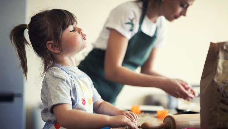 Cute little girl baking at home with mom, young mother and daughter making cookies in the kitchen.