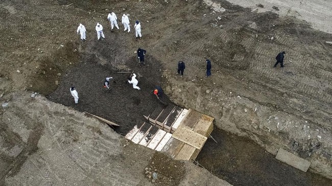 Workers wearing personal protective equipment bury bodies in a trench on Hart Island, Thursday, April 9, 2020, in the Bronx borough of New York. On Thursday, New York City’s medical examiner confirmed that the city has shortened the amount of time it will hold on to remains to 14 days from 30 days before they will be transferred for temporary internment at a City Cemetery. Earlier in the week, Mayor Bill DeBlasio said that officials have explored the possibility of temporary burials on Hart Island, a strip of land in Long Island Sound that has long served as the city’s potter’s field.  (AP Photo/John Minchillo)