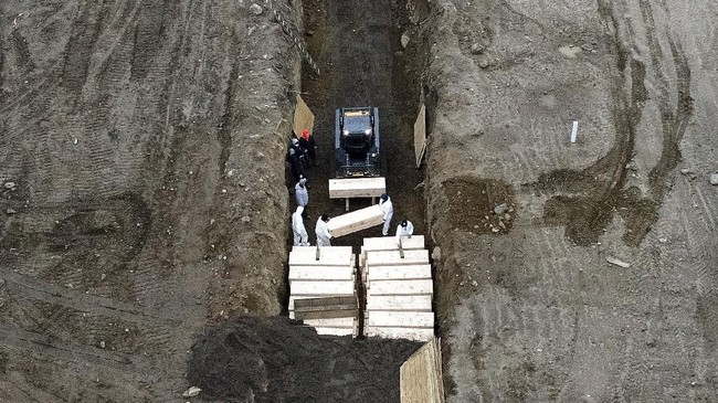Workers wearing personal protective equipment bury bodies in a trench on Hart Island, Thursday, April 9, 2020, in the Bronx borough of New York. On Thursday, New York City's medical examiner confirmed that the city has shortened the amount of time it will hold on to remains to 14 days from 30 days before they will be transferred for temporary internment at a City Cemetery. Earlier in the week, Mayor Bill DeBlasio said that officials have explored the possibility of temporary burials on Hart Island, a strip of land in Long Island Sound that has long served as the city's potter's field. (AP Photo/John Minchillo)