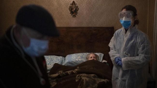 Josefa Ribas, 86, who is bedridden, looks at nurse Alba Rodriguez as Ribas’ husband, Jose Marcos, 89, stands by in their home in Barcelona, Spain, March 30, 2020, during the coronavirus outbreak. Ribas suffers from dementia, and Marcos fears for them both if the virus enters their home. 