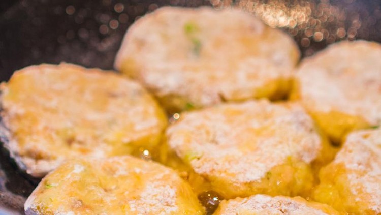 Close-up of round crab and fish cakes made with sweet potatoes and vegetables frying in a blue cast iron pan.