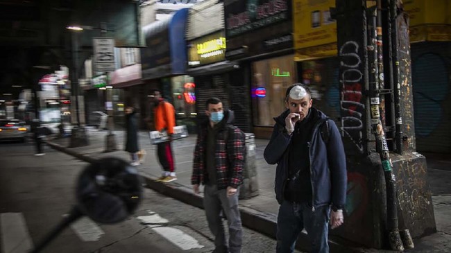A man smokes a cigarette while waiting to cross a street in the Brooklyn borough of New York, on Wednesday, March 25, 2020. (AP Photo/Wong Maye-E)