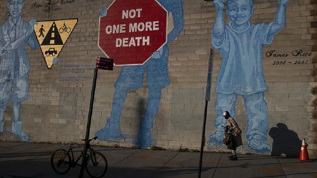 A woman with a face mask walks past a mural in the Brooklyn borough of New York, on Friday, March 27, 2020. (AP Photo/Wong Maye-E)