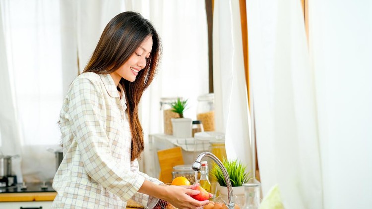 Asian beautiful teen girl is washing the apple and other fruit in the kitchen and look happy.