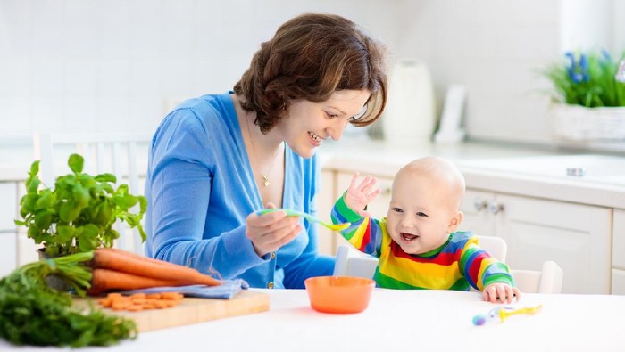 Mother feeding child. First solid food for young kid. Fresh organic carrot for vegetable lunch. Baby weaning. Mom and little boy eat vegetables. Healthy nutrition for children. Parents feed kids.