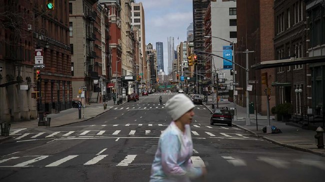 A cyclist rides down the center of Hudson Street, free of traffic, as a woman crosses in New York, on Sunday, March 22, 2020. (AP Photo/Wong Maye-E)