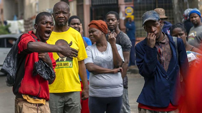 People living near the traditional medicine market wait to receive food baskets from private donors, Monday, April 13, 2020 downtown Johannesburg. Because of South Africa's imposed lockdown to contain the spread of COVID-19, many are not able to work. The new coronavirus causes mild or moderate symptoms for most people, but for some, especially older adults and people with existing health problems, it can cause more severe illness or death.(AP Photo/Jerome Delay)