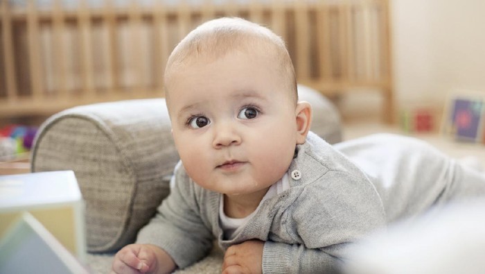 Charming beautiful lovely small female baby with plump cheeks creeps on bed, looks innocently on something, being naughty. Cute baby infant plays alone. Newborn kid crawls. Enthusiastic child