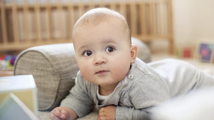 Charming beautiful lovely small female baby with plump cheeks creeps on bed, looks innocently on something, being naughty. Cute baby infant plays alone. Newborn kid crawls. Enthusiastic child
